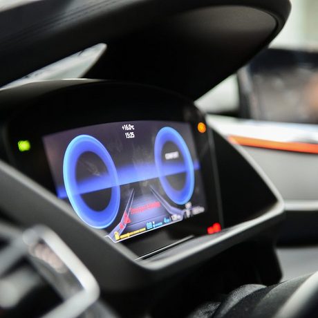 Blick in das Cockpit von einem Fahrzeug mit digitalem Tachometer. Im Hintergrund ist das Armaturenbrett der Beifahrerseite zu sehen.