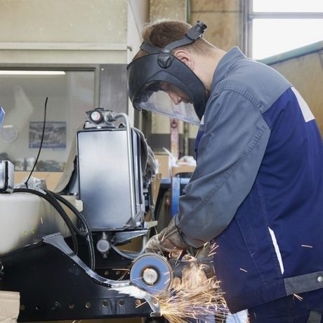 Ein Mechaniker in Schutzkleidung bearbeitet Metall mit einem Winkelschleifer. (Foto: Bundesagentur für Arbeit)