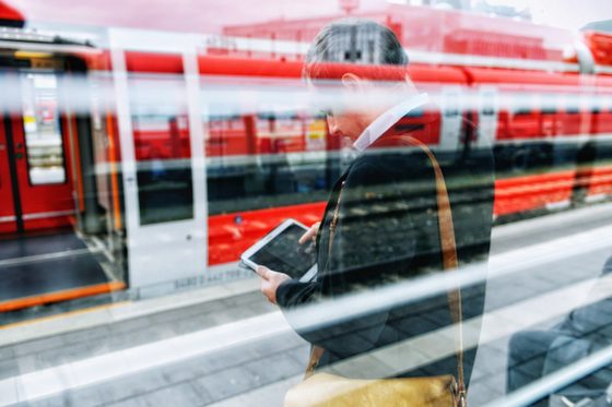 Ein junger Mann steht an einem Gleis und guckt auf sein Tablet. Foto: Julien Fertl