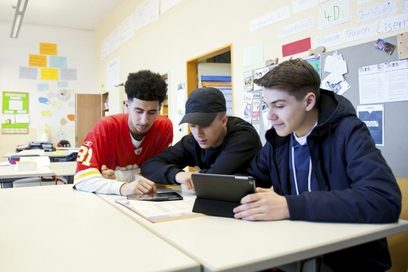 Drei Schüler sitzen am Tisch und sehen auf Tablets.