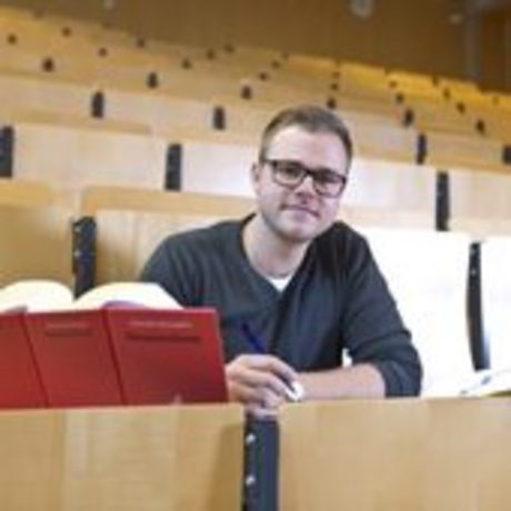 Ein Student sitzt im Hörsaal vor einem geöffneten Buch.