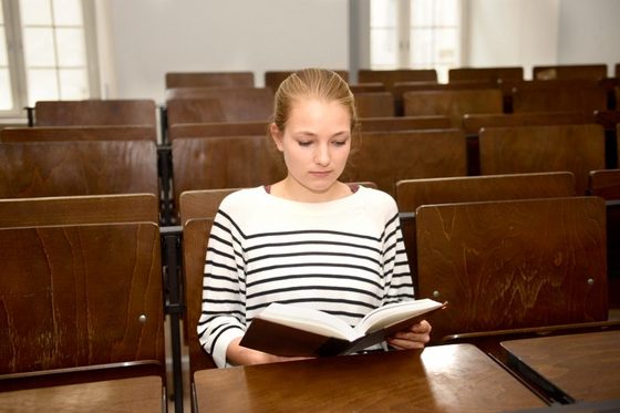 Eine junge Frau sitzt in einem Hörsaal und liest in einem Buch.