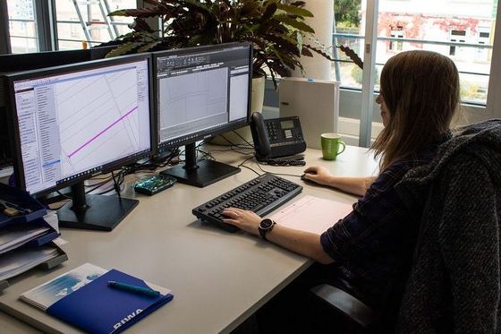 Eine junge Frau sitzt an einem Schreibtisch und bearbeitet an zwei Computerbildschirmen Kartenausschnitte.