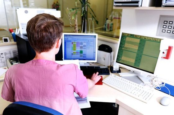 Junger Krankenpfleger sitzt an einem Schreibtisch und gibt Daten in einen Computer ein
