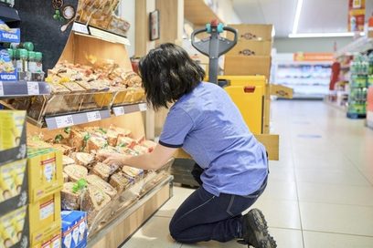 Eine Frau räumt Waren in ein Supermarkt-Regal ein.