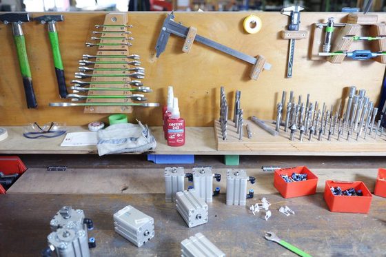 Blick auf eine Werkbank mit verschiedenen Werkzeugen, wie Schraubenschlüssel, Bohrer und Hämmer.