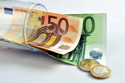 Ein liegendes Glas, aus welchem ein 50-Euro-Gelschein und ein 100-Euro-Geldschein sowie zwei Münzen herauslugen.