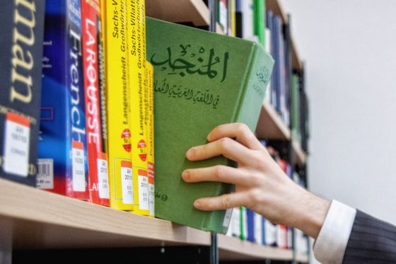 Ein Mann greift nach einem arabischen Sprachbuch in einem Bücherregal. (Foto: Sonja Trabandt)
