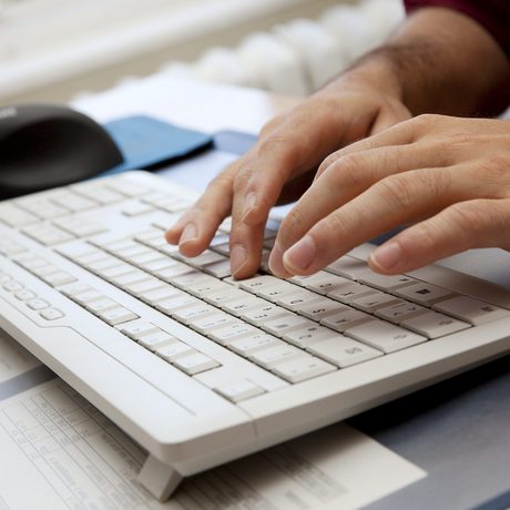 Hände eines Manns tippen auf einer weißen Computer-Tastatur.