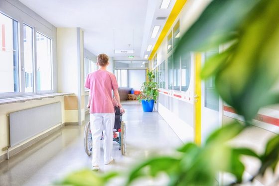 Krankenpfleger fährt Patientin in einem Rollstuhl durch das Krankenhaus. Foto: Martin Rehm