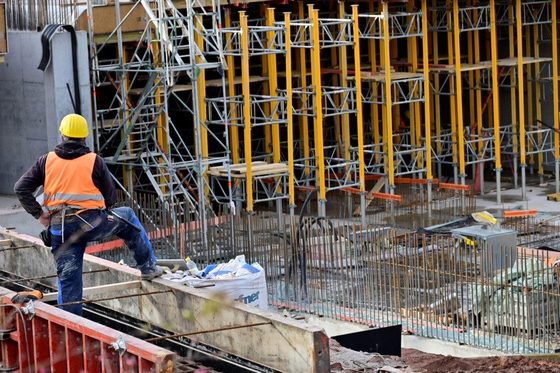 Ein Bauarbeiter mit einer Warnweste steht auf einer Baustelle und schaut sich eine Stahlbetonkonstruktion an. Man sieht ihn nur von hinten.