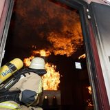 Ein junger Mann mit Schutzanzug und Feuerwehrausrüstung löscht einen Übungsbrand im Übungscontainer.
