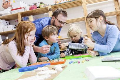 Ein Mann erklärt vier Kindern am Tisch ein Spiel. (Foto: Robert Söllner | Bundesagentur für Arbeit)
