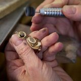 Nahaufnahme der Hände einer Goldschmiedin, die einen Goldohrring aus dem 19. Jahrhundert an einem Werktisch poliert.