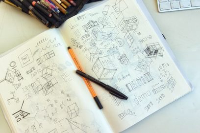 Das Foto zeigt ein aufgeschlagenes Notizbuch mit vielen Skizzen und Zeichnungen. Im Falz liegen zwei Stifte.