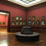 Blick in einen roten Saal der Gemäldegalerie Dresden mit vielen Portraitbildern an den Wänden und einer braunen Rundcouch in der Mitte. (Foto: Bundesagentur für Arbeit)