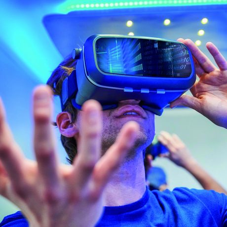 Ein Mann blickt durch eine VR-Brille und hat die Hand erhoben.