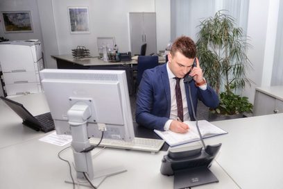 Ein junger Mann sitzt an einem Büroarbeitsplatz und telefoniert.