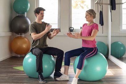 Ein Mann zeigt einer Frau eine Übung mit Gymnastikbällen.