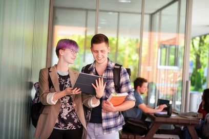 Ein Student und eine Studentin stehen in einer Uni und blicken gemeinsam auf ei Tablet