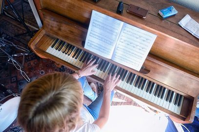Aus der Vogelperspektive ist ein Klavier zu sehen sowie die blonden Haare einer Frau, deren Finger auf der Tastatur liegen.