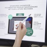 Bildschirm auf dem ein offener Laptop abgebildet wird mit Vorschlägen für Werbemaßnahmen eines Showrooms. Davor hält eine Hand einen Stift und zeigt auf den Punkt "Verlinkung zum Online-Shop.