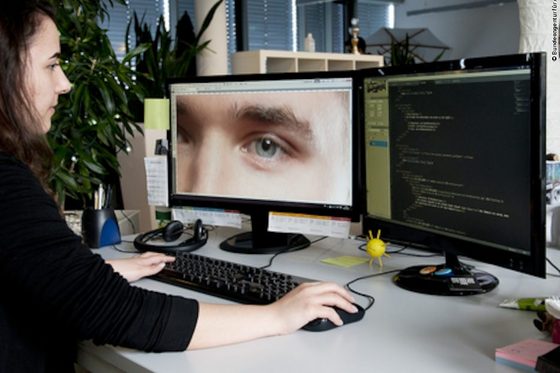 Eine Frau sitzt am Schreibtisch vor einem Computerbildschirm und chattet mit einem Mann über eine Chatplattform.