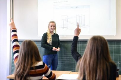 Junge Lehrerin unterrichtet an einem Whiteboard in einem Klassenzimmer.