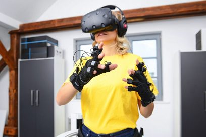 Eine Frau trägt eine Virtual-Reality-Brille und Fingerhandschuhen mit Sensoren