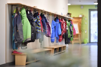 Mehrere Kinderjacken hängen an einer Garderobe im Flur eines Kindergartens.
