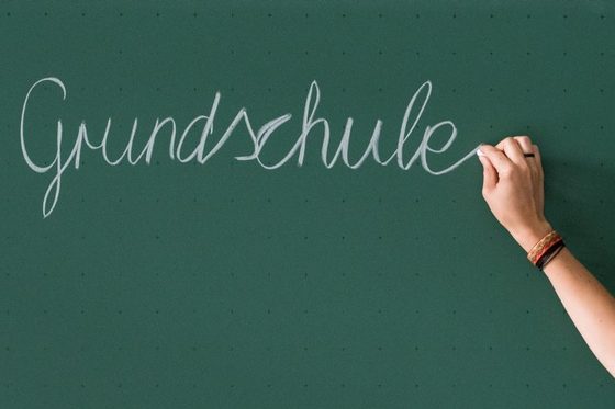 Eine Hand schreibt das Wort "Grundschule" an die Tafel.
