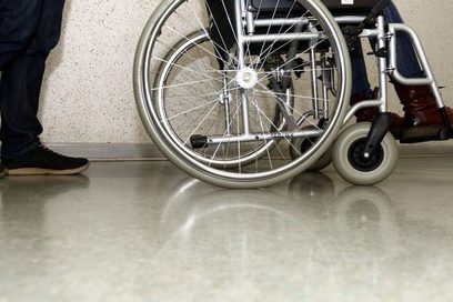 Ein junger Mann fährt behinderte junge Frau mit einem Rollstuhl durch ein Gebäude. (Foto: Martin Rehm)