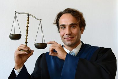 Jurist in Robe hält eine Waage in der Hand. Foto: Christof Stache
