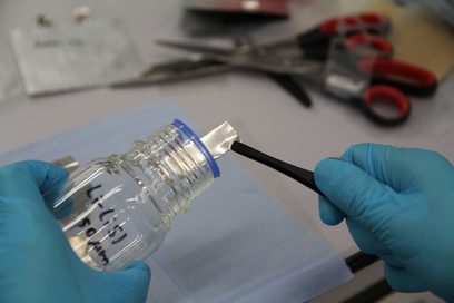 Jemand holt mit einer Pinzette einen Lithiumstreifen aus einem Glas.