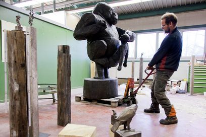 ein Mann nimmt mit einem Palettenwagen die lebensgroße Holzfigur eines Gorillas auf.