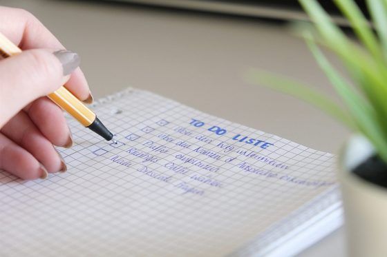 Die Hand einer Frau schreibt eine TO DO Liste auf einen Notizblock.