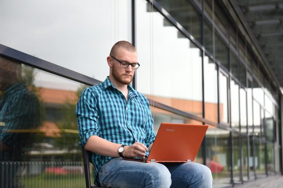 Ein junger Mann sitzt draußen auf einem Stuhl und schaut in einen Laptop.