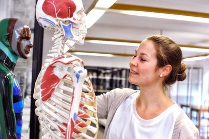Eine junge Frau betrachtet ein anatomisches Modell eines menschlichen Körpers.