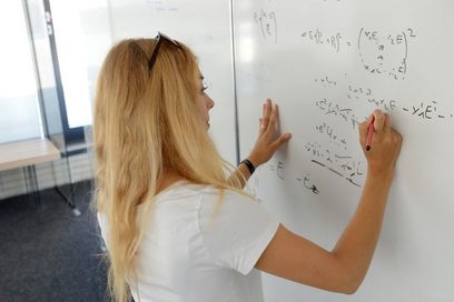 Eine junge Frau führt physikalische Berechnungen an einem Whiteboard durch.