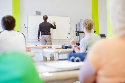 Ein Lehrer steht vor einer Klasse und schreibt an die Tafel. (Foto: Michael Neuner)