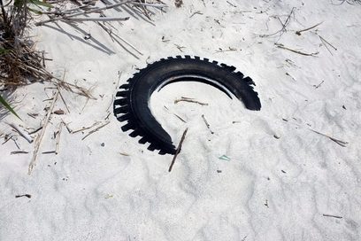 Das Bild zeigt einen halb sandbedeckten Traktorreifen an einem Strand.