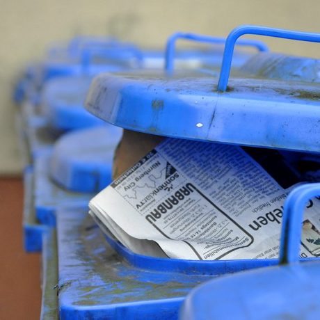 Blaue Recycling-Mülltonnen für Papier stehen hintereinander aufgereiht.