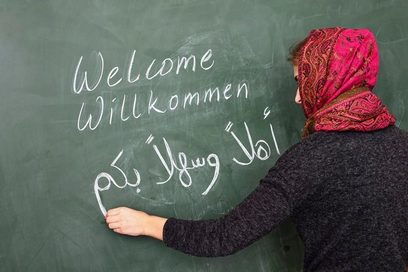 Frau mit Kopftuch schreibt Welcome, Willkommen und Willkommen in arabischer Sprache an eine Tafel.