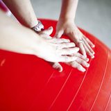 Eine Physiotherapeutische Situation: vier Hände, die auf einen roten Ball drücken
